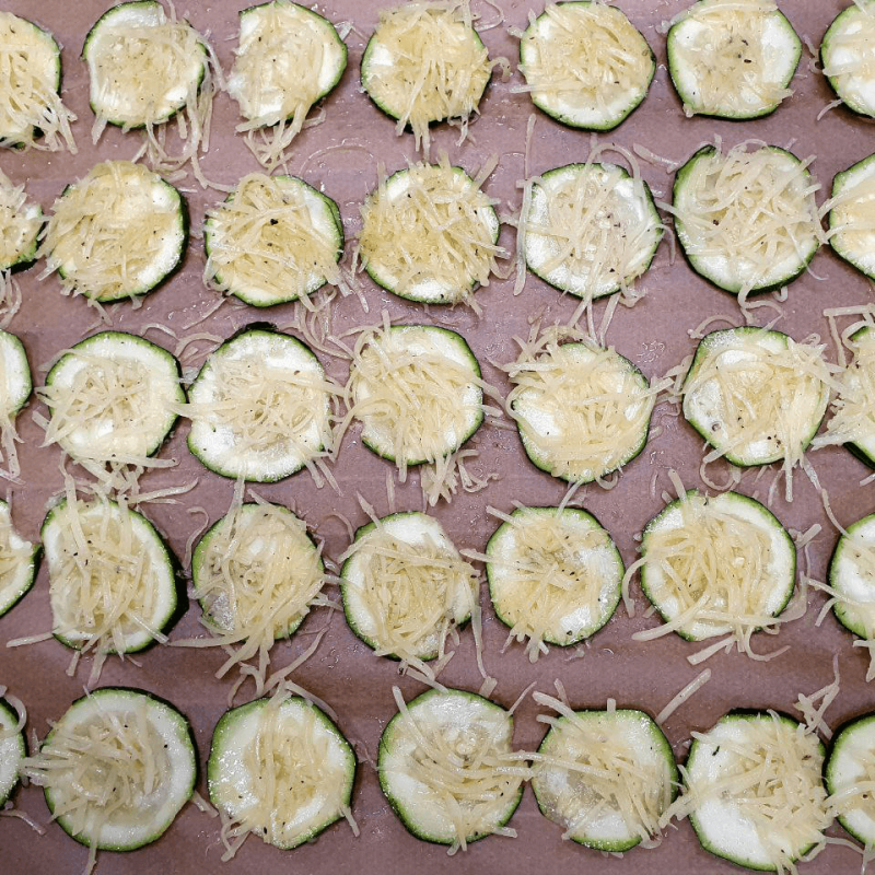 Zucchinischeiben mit Käse darauf auf einem Backblech aneinander gereiht