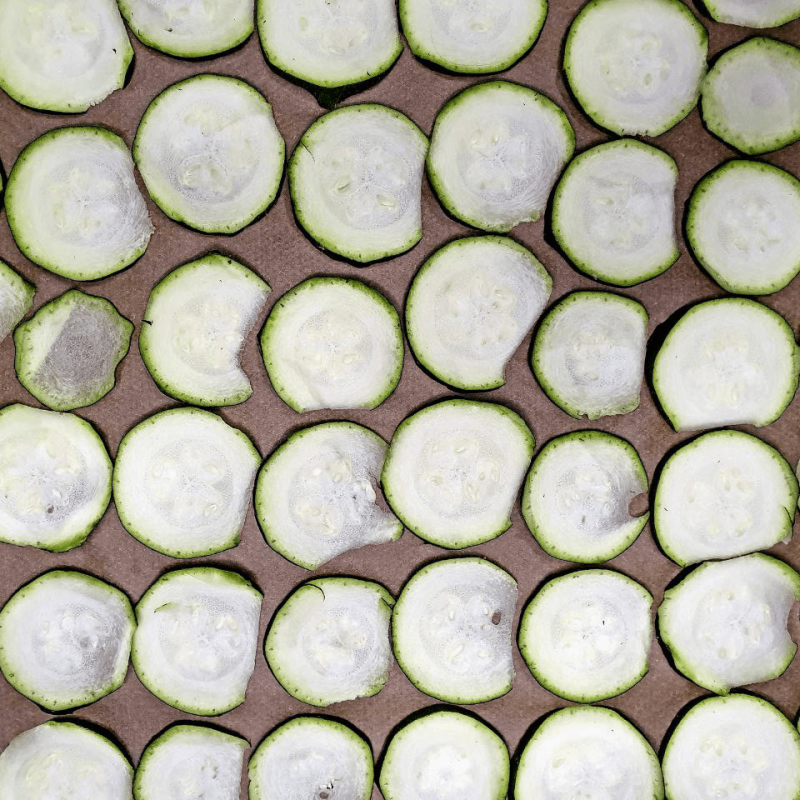 Man sieht Zucchinischeiben aufgereiht auf einem Backblech nebeneinander liegen